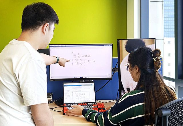Two MathWorks employees look at a computer screen while one points to a particular area on the screen.