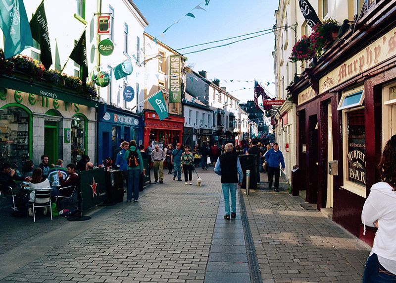 People walking along a pedestrian street. It is full of shops, pubs, and restaurants.