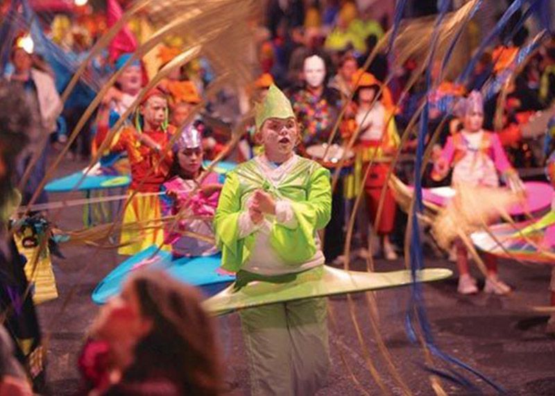 A boy dressed in a green costume and hat walks with other costumed children as part of a Halloween festival.