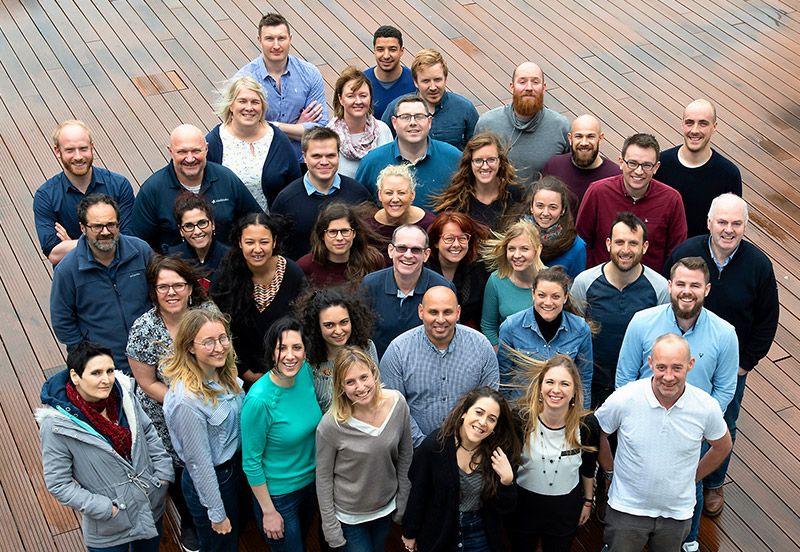 Three dozen Galway employees stand together on an outside deck and smile up at the camera.
