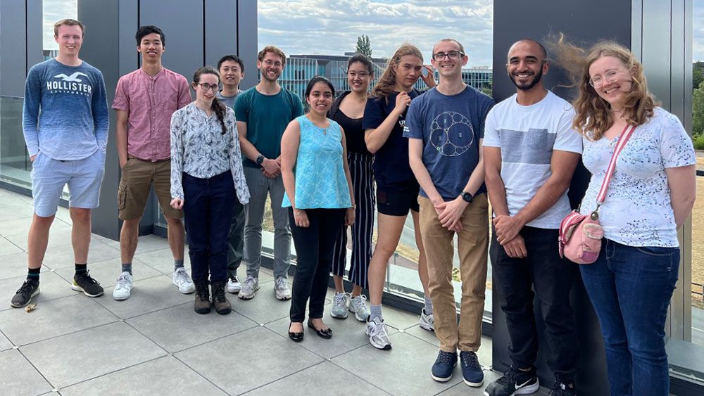 Group photo showing MathWorks staff in casual clothing on a modern rooftop with office building and blue sky in the background.